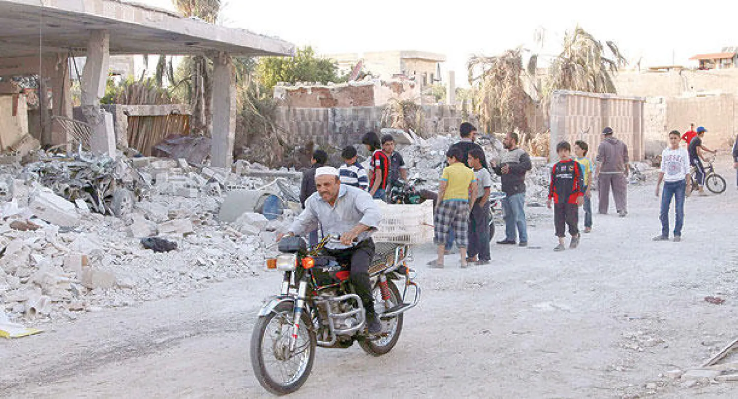 صورة وزعت أمس لسوري على متن دراجة نارية، بينما يعاين آخرون ما خلفه برميل متفجر  -سقط على مبنى في قرية كحيل بريف درعا (رويترز)