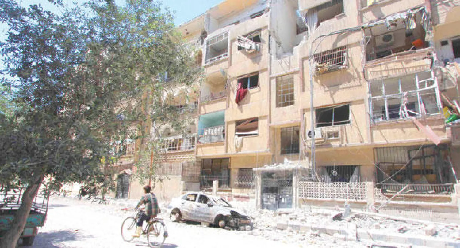 سوري يمر بدراجته الهوائية في أحد شوارع بلدة المليحة بريف دمشق، أمس، بينما تظهر واجهات الأبنية مدمرة جراء المعارك بين النظام والمعارضة (رويترز)