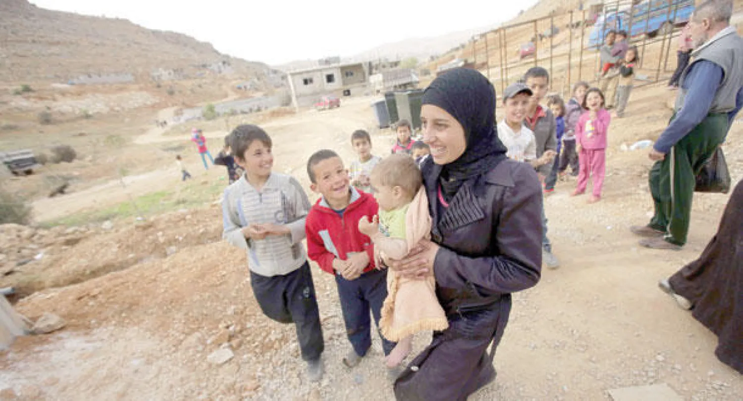 سورية تحمل طفلها في مخيم اللاجئين في مدينة عرسال اللبنانية (أ.ف.ب)