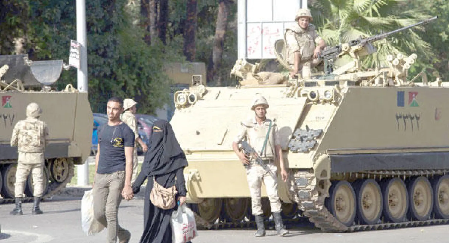 مواطن مصري وزوجته يسيران بجوار مدرعة أمام جامعة القاهرة في محافظة الجيزة أمس (أ.ف.ب)