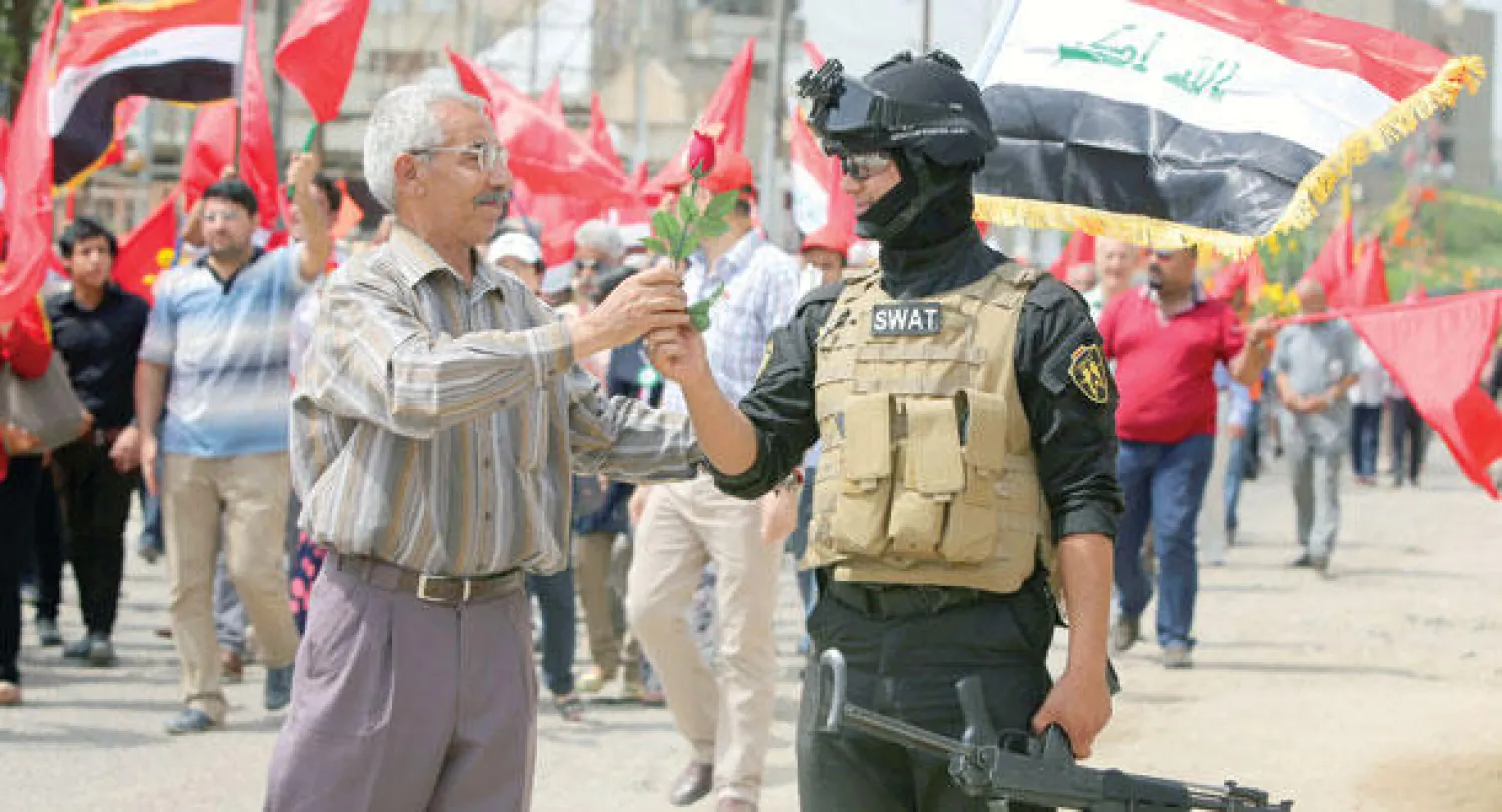 عراقي يقدم زهرة لعنصر أمن وسط بغداد أمس ضمن مسيرة للاحتفال بيوم العمال (أ.ف.ب)