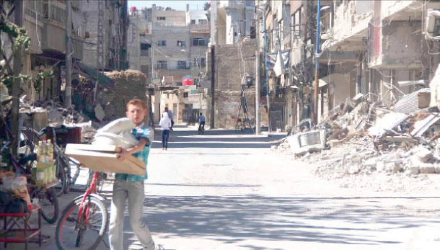 صورة وزعت أمس لصبي سوري يمر في شارع تعرض لأضرار جسيمة في زملكا بريف دمشق (رويترز)