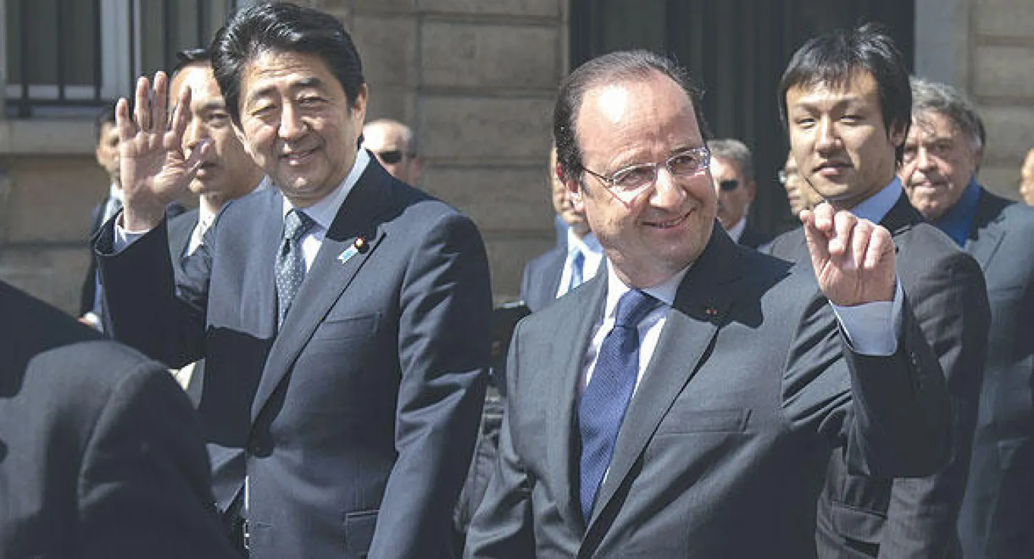 الرئيس الفرنسي فرنسوا هولاند بجوار رئيس وزراء اليابان شينزو آبى الذي يزور باريس حاليا  يحييان الجماهير في شوارع  العاصمة باريس عقب مغادرتهما قصر الإليزيه سيرا على الأقدام (أ.ب)