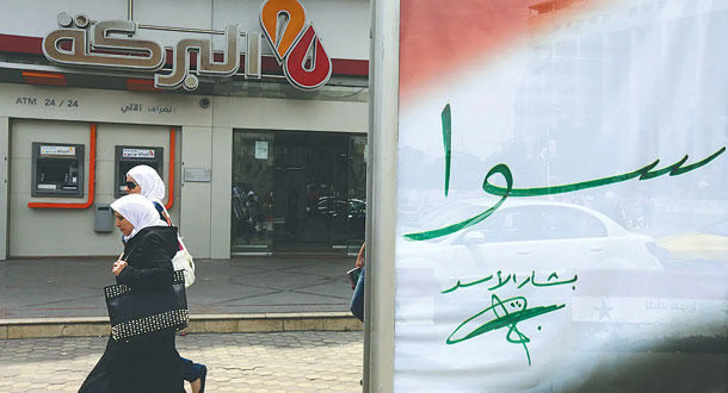 سوريتان تسيران قرب ملصق انتخابي في دمشق يروج للرئيس السوري بشار الأسد  الذي أطلق حملته تحت شعار «سوا» (أ.ف.ب)