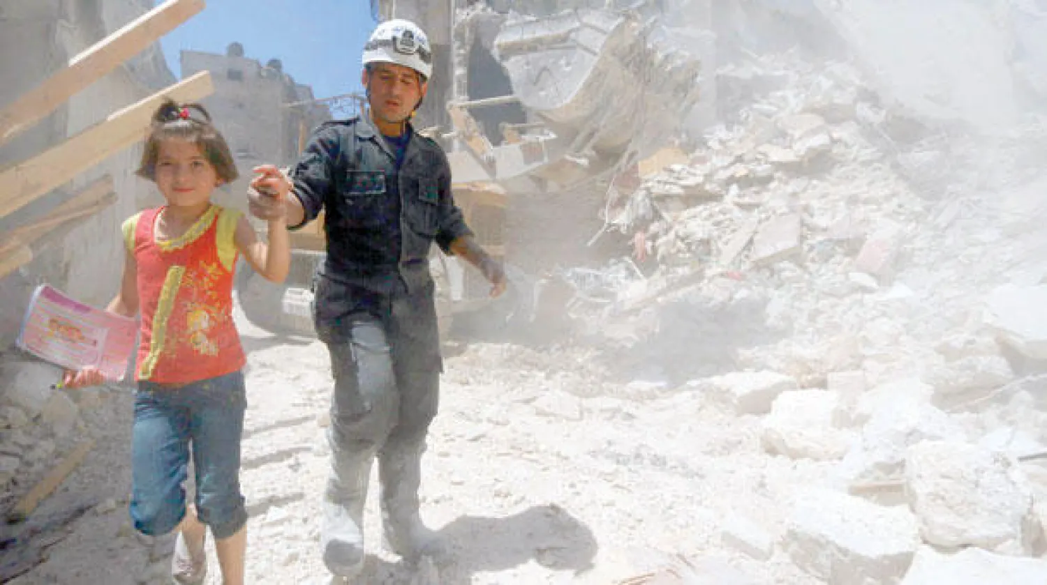 عنصر في الدفاع المدني يخلي طفلة من مبنى بعد استهدافه من الطيران الحربي النظامي في حي الكلاسة بحلب أمس (رويترز)