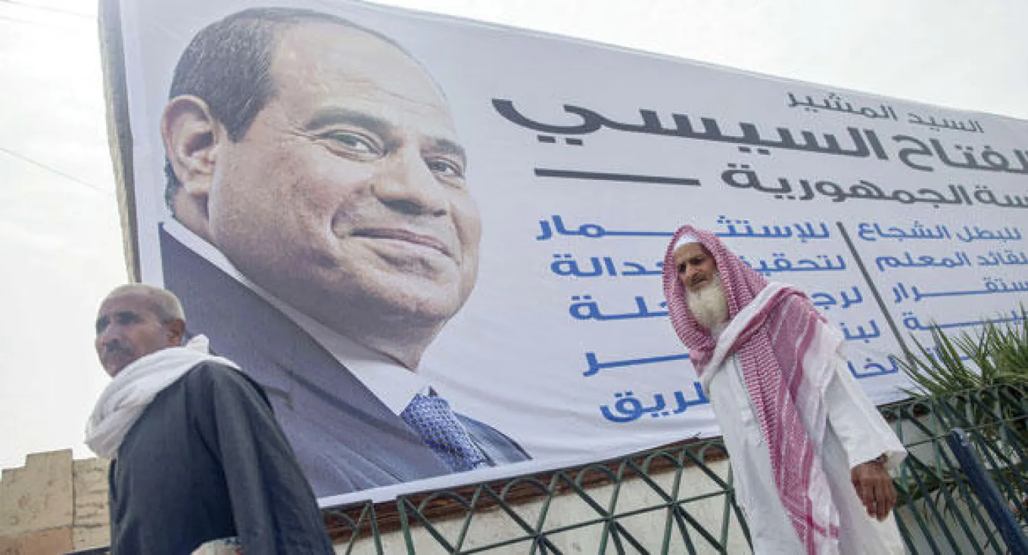 مصريان يسيران بجوار ملصق دعائي ضخم يدعو لانتخاب  السيسي (أ ف ب)