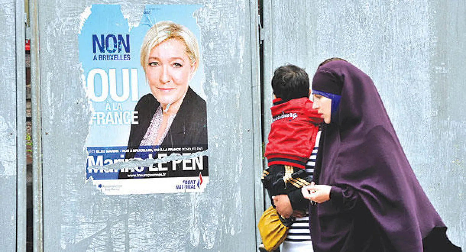 امرأتان تحمل إحداهما رضيعا تمران أمام صورة دعائية لزعيمة اليمين المتطرف مارين لوبن في مدينة دونين بشمال فرنسا أمس (أ.ف.ب)