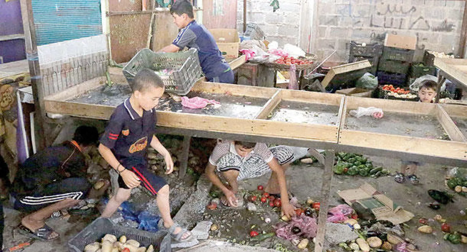 أطفال عراقيون يجمعون بعض الطماطم والبطاطا والخضار من الأرض بعد تفجير سوق في مدينة الصدر شرق بغداد أمس(أ.ب)