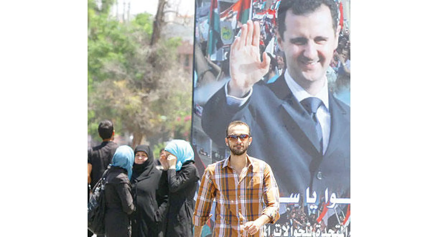 مواطن سوري يمر بجوار ملصق دعائي للرئيس الأسد  في وسط العاصمة دمشق أمس (أ.ف.ب)