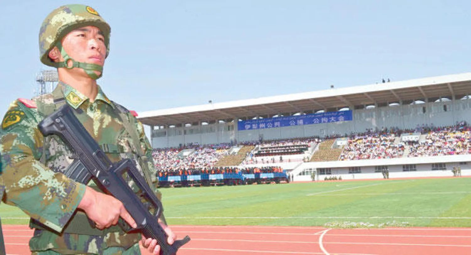 عسكري يحرس شاحنات تنقل عشرات المتهمين لمحاكمتهم في ملعب كرة قدمبمنطقة ييلي في إقليم شينجيانغ أمس (رويترز)