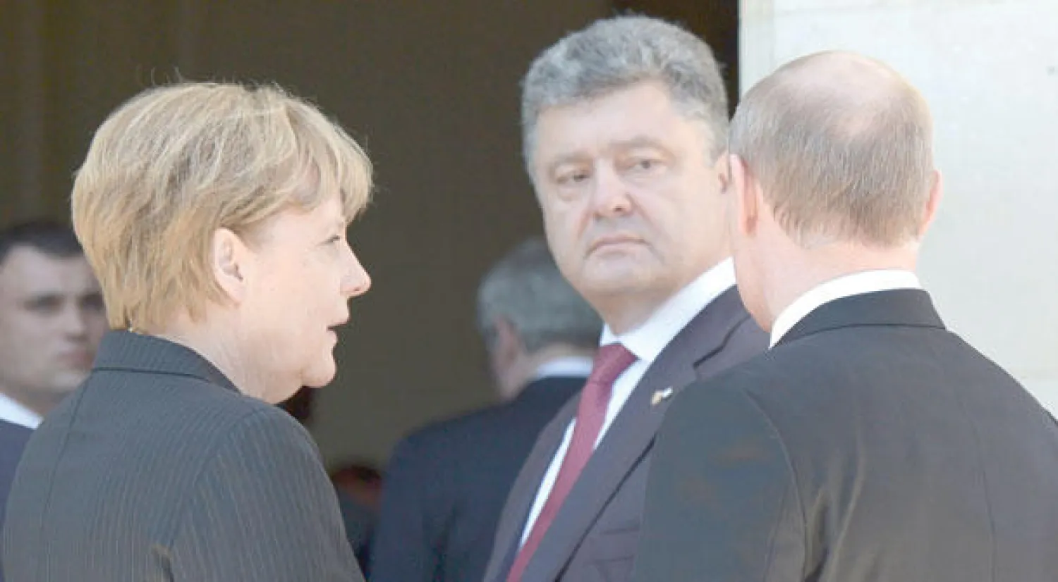 الرئيس الأوكراني المنتخب بوروشينكو (وسط) ينظر إلى الرئيس الروسي بوتين وتبدو بينهما المستشارة الألمانية ميركل على هامش الاحتفال بذكرى الإنزال في النورماندي أمس (رويترز)