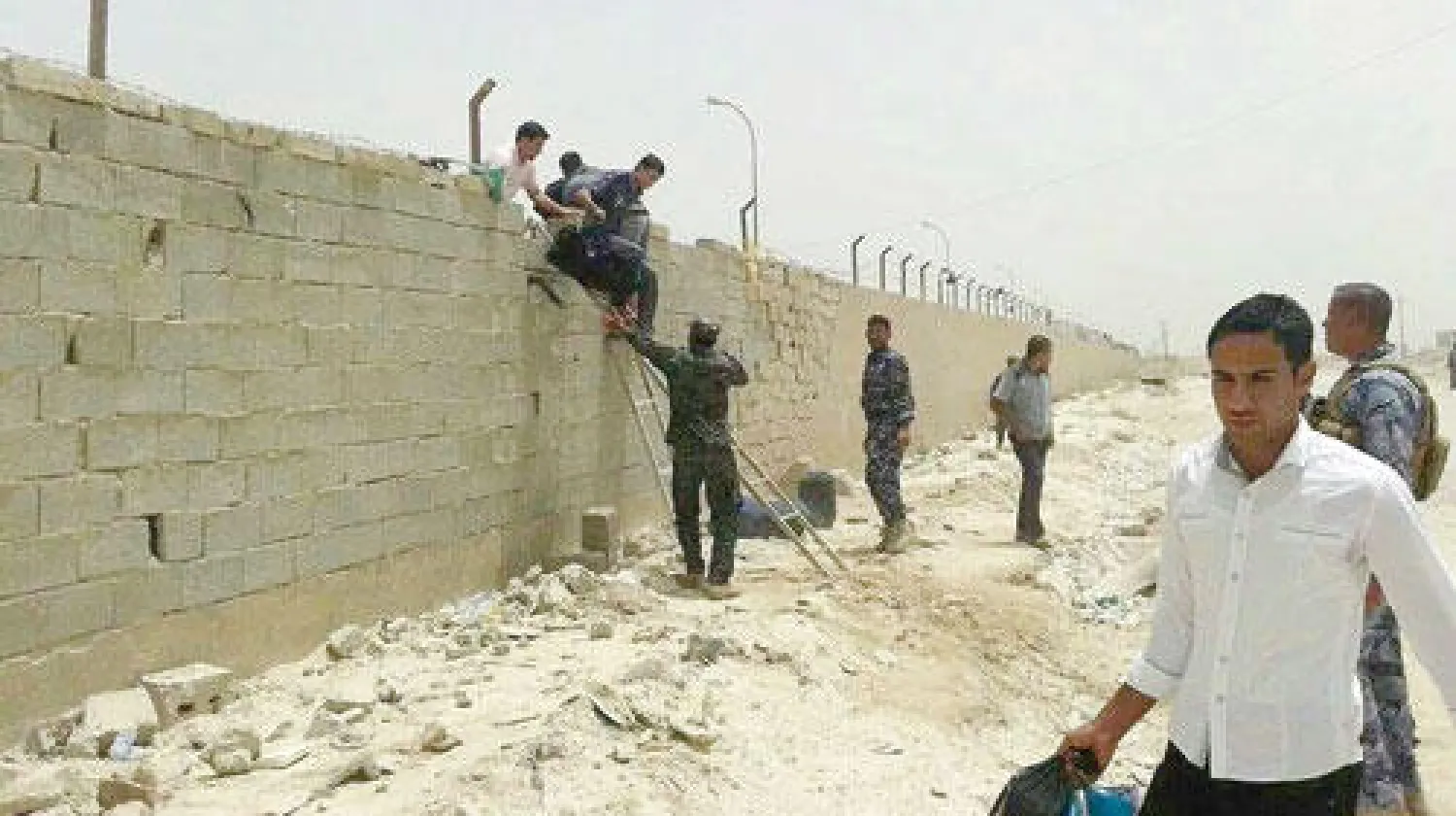 طلاب يقفزون من فوق سور جامعة الأنبار في الرمادي هاربين من مسلحي «داعش» الذين اقتحموها أمس (إ.ب.أ)