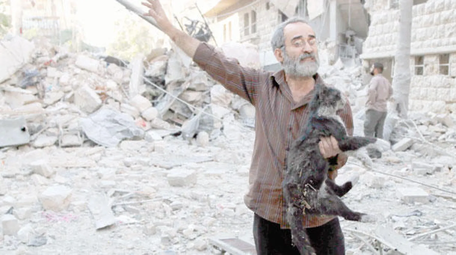 سوري يحمل قطة بعد أن أنقذها من بين ركام مبنى دُمِّر جراء قصف حكومي ببرميل متفجر استهدف حي بستان القصر في حلب أمس (رويترز)