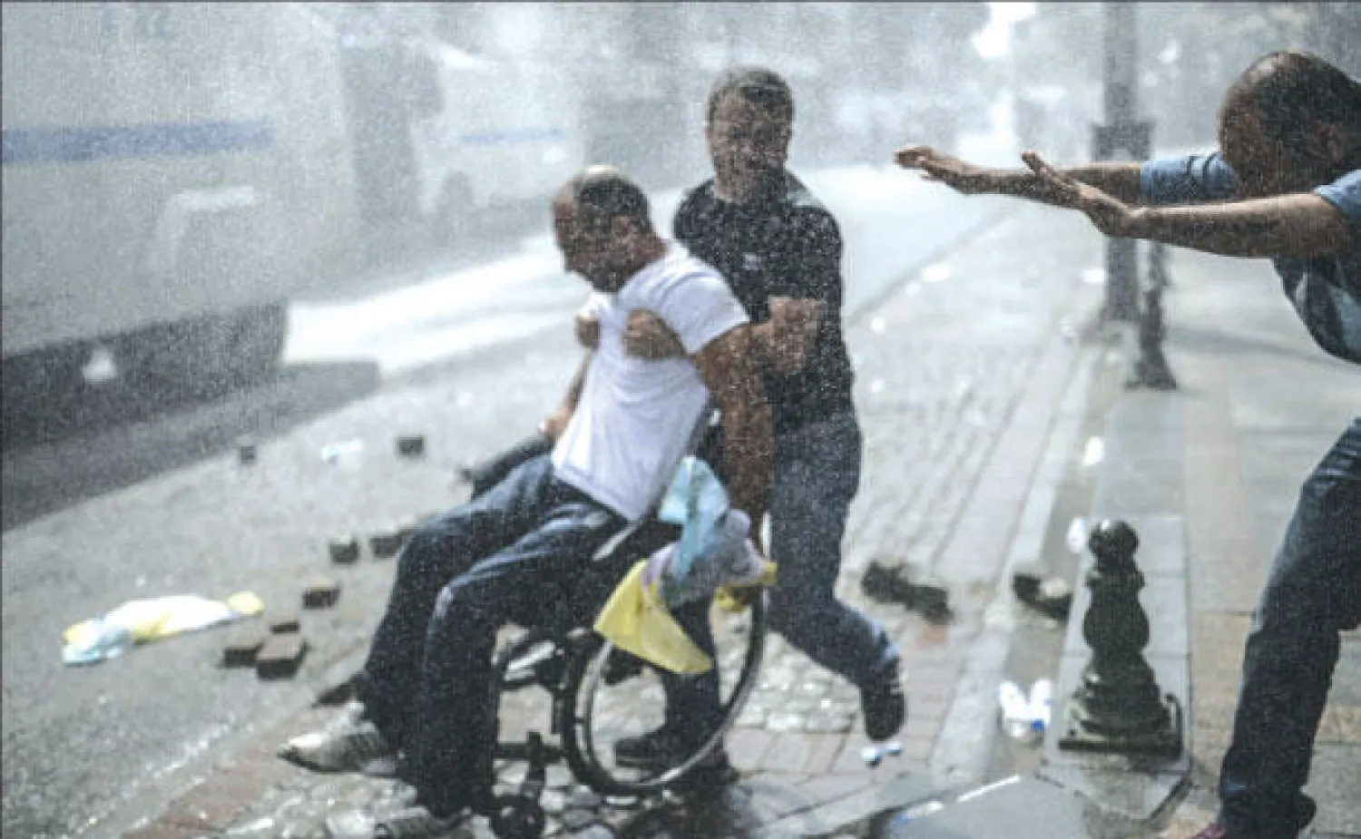 شخصان يهبان لمساعدة آخر على كرسي متحرك خلال مواجهات بين محتجين أكراد وشرطة مكافحة الشغب التركية في إسطنبول أمس (أ.ف.ب)