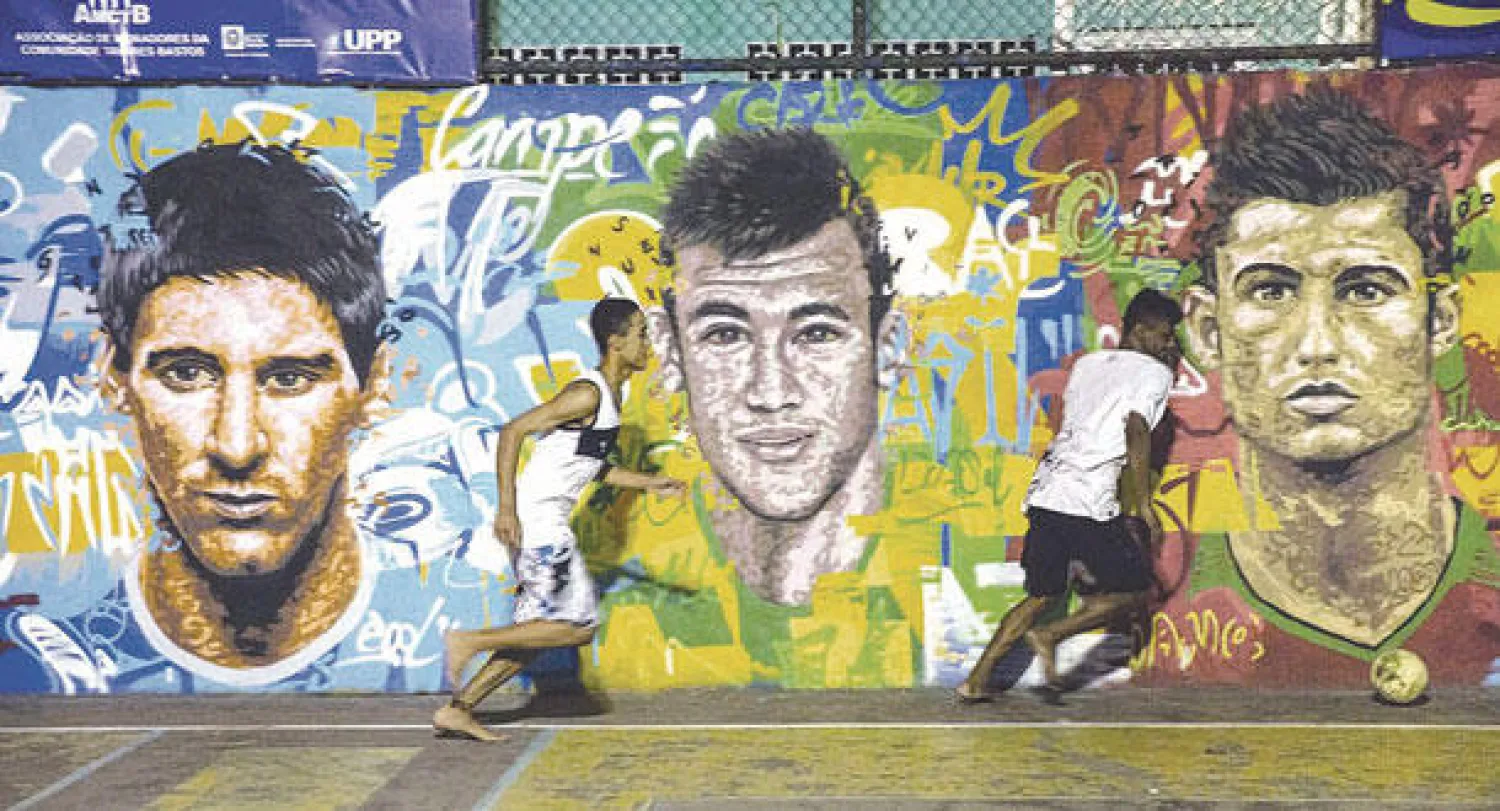 برازيليون يلعبون الكرة أمام حائط حمل رسوما للنجوم الأكثر شعبية في العالم نيمار وميسي ورونالدو