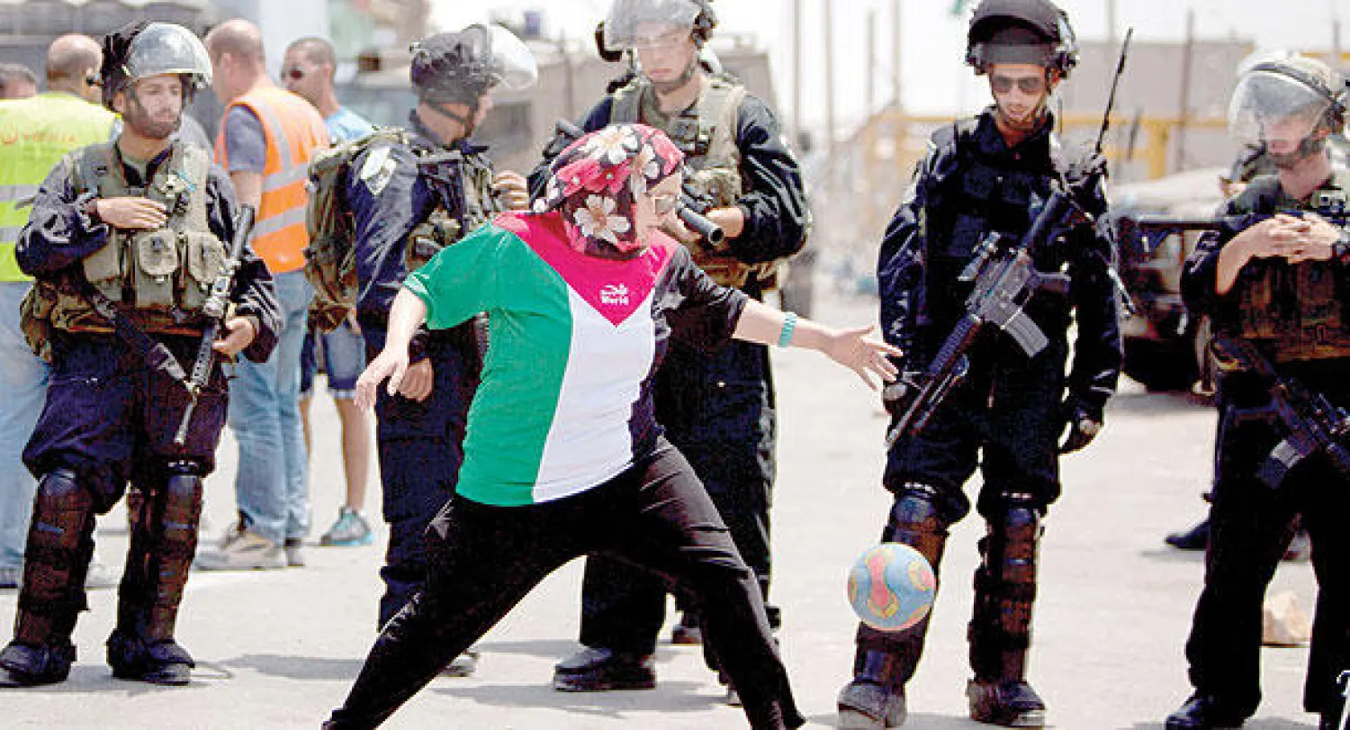 فلسطينية تلعب كرة القدم أمام جنود إسرائيليين خلال مظاهرة احتجاج قبالة سجن عوفر، في الضفة الغربية، أمس، للمطالبة بإطلاق سراح الأسرى المضربين عن الطعام (أ.ب)