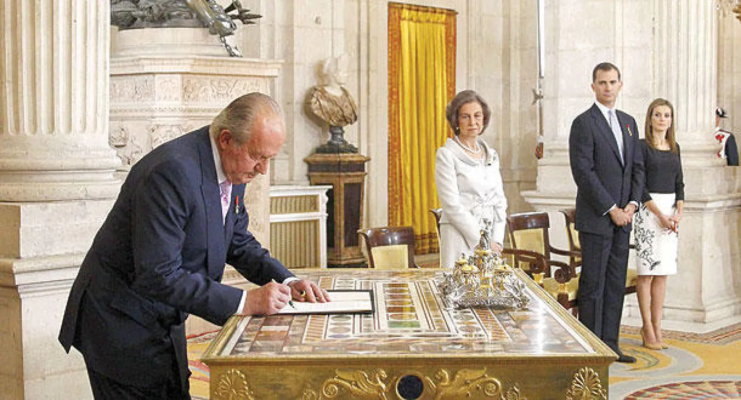 الملك خوان كارلوس يوقع على قانون تنازله عن العرش بينما تبدو الملكة صوفيا  ونجلها الأمير فيليبي والأميرة لتيثيا في القصر الملكي بمدريد أمس (إ.ب.أ)