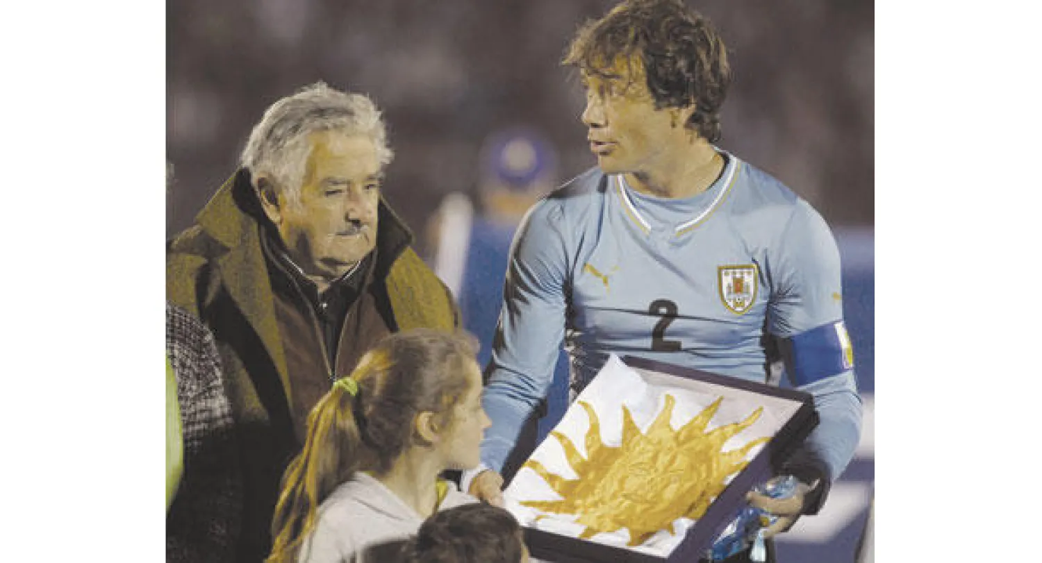 رئيس الأوروغواي موخيكا يقدم علم بلاده لجودين قائد المنتخب (أ.ب)