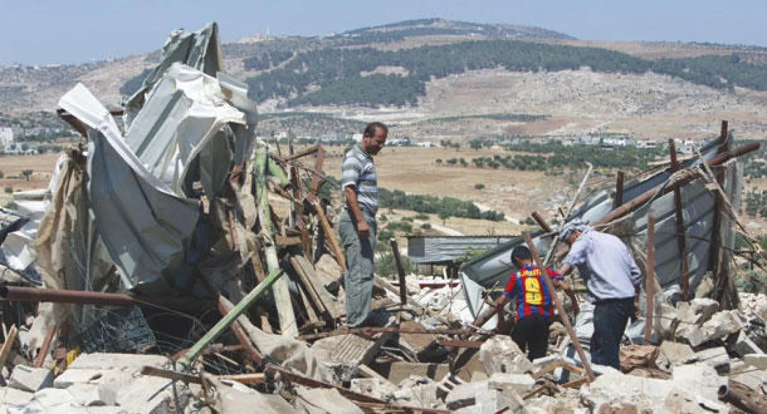 فلسطينيون يسيرون على ركام منزلهم الذي دمرته القوات الإسرائيلية أمس (أ.ب)