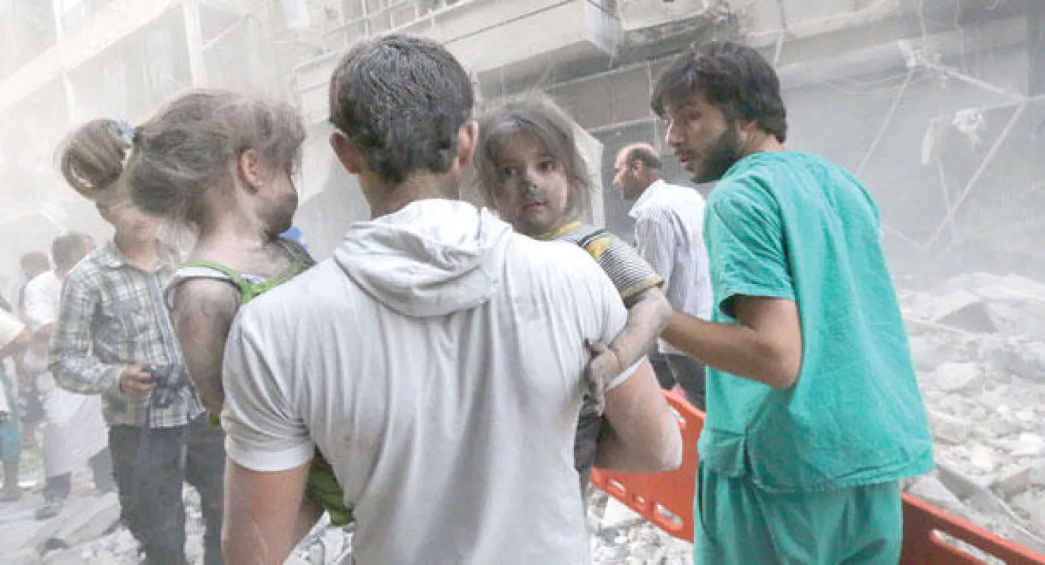 سوري يحمل طفلتين يغمر غبار أسود وجهيهما بعد قصف النظام لمنطقة سكنية في حلب (أ.ف.ب)