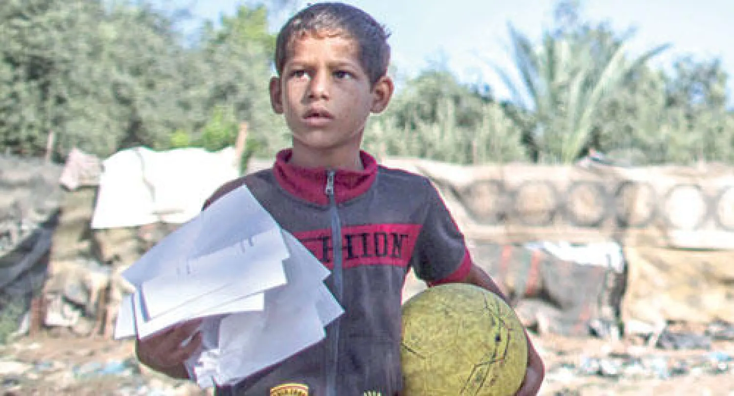طفل يحمل منشورا وزعته اسرائيل يطالب الفلسطينيين بمغادرة منازلهم في غزة أمس (إ.ب.أ)