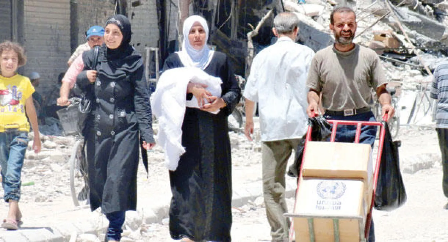 عائلة سورية تنقل صناديق حصلت عليها من منظمة الإغاثة الدولية والأونروا في مخيم اليرموك أمس (أ.ف.ب)