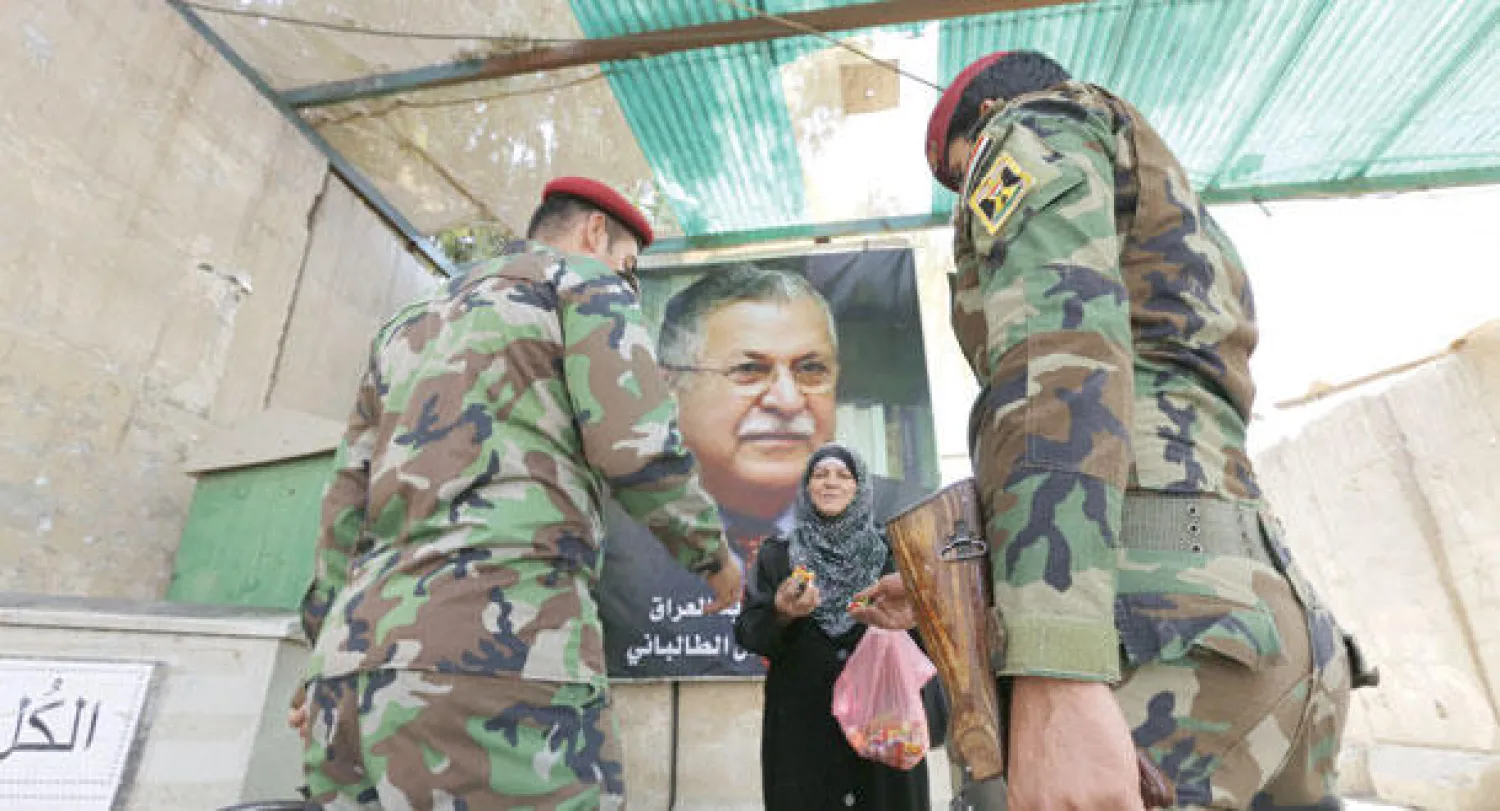 عراقية تقدم أمس حلويات لجنديين يحرسان مقر حزب الاتحاد الوطني الكردستاني في بغداد بمناسبة عودة زعيم الحزب الرئيس العراقي جلال طالباني من رحلة العلاج إلى ألمانيا (أ.ف.ب)