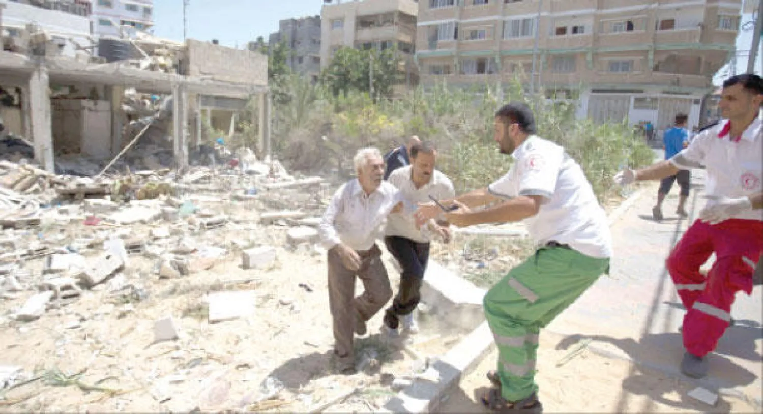 طواقم طبية تساعد فلسطينيا انتشلته من تحت الأنقاض بعد غارة إسرائيلية على غزة أمس (أ.ف.ب)