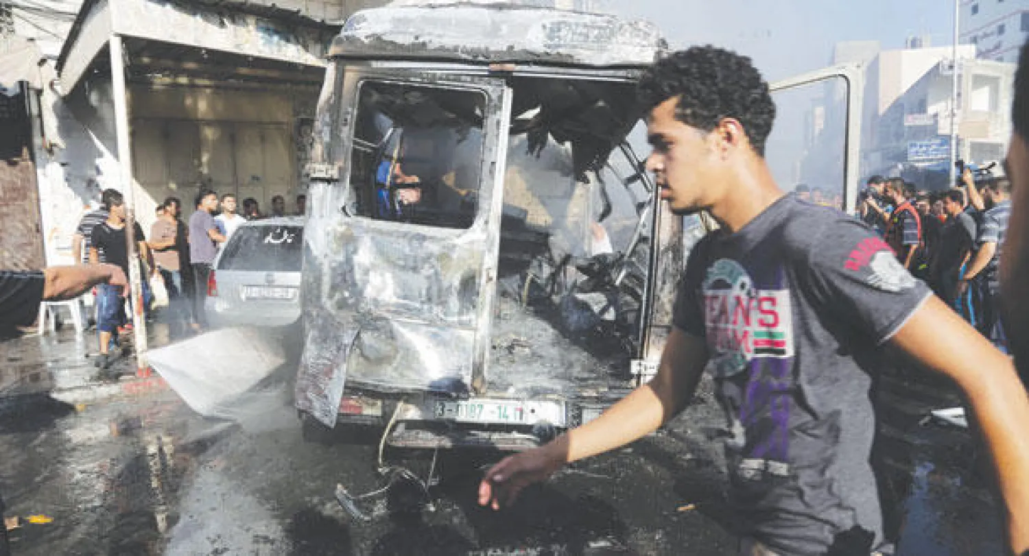 فلسطيني يقطع الشارع وتبدو خلفه سيارة محترقة جراء القصف الإسرائيلي على غزة أمس (أ.ب)