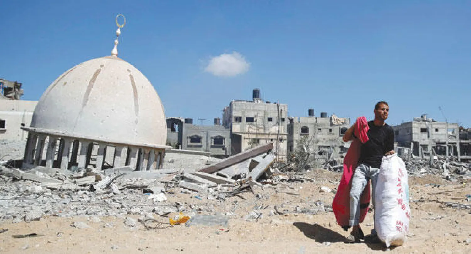 فلسطيني يحمل أغراضا في بلدة خزاعة التي تعرضت لغارات إسرائيلية دُمر خلالها مسجد أمس (رويترز)