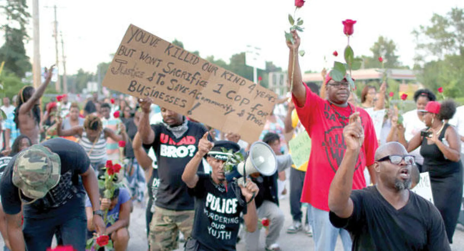 متظاهرون يحملون ورودا خلال الاحتجاج على مقتل الشاب مايكل براون في فيرغسون أمس.. وتقول اللافتة للشرطة «انتم قتلتمونا لسنوات ولكن لن تضحوا برجل شرطة واحد لتحقيق العدالة وحماية المجتمع»  (أ.ف.ب)