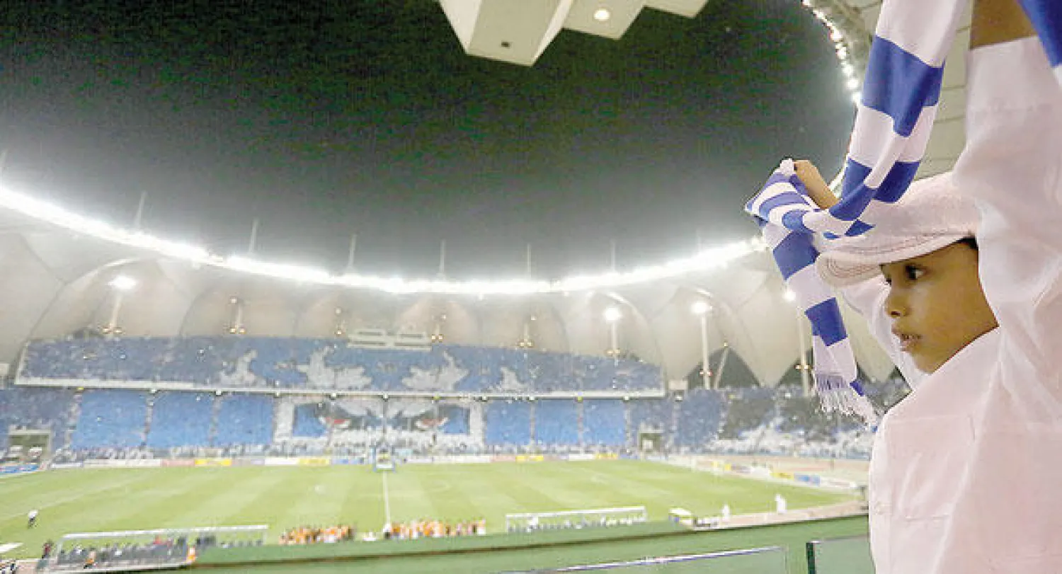 طفل هلالي يساند فريقه أمام السد القطري بينما يظهر تيفو الجماهير في مدرجات الدرجة الثانية قبل انطلاق المواجهة (تصوير: علي العريفي)