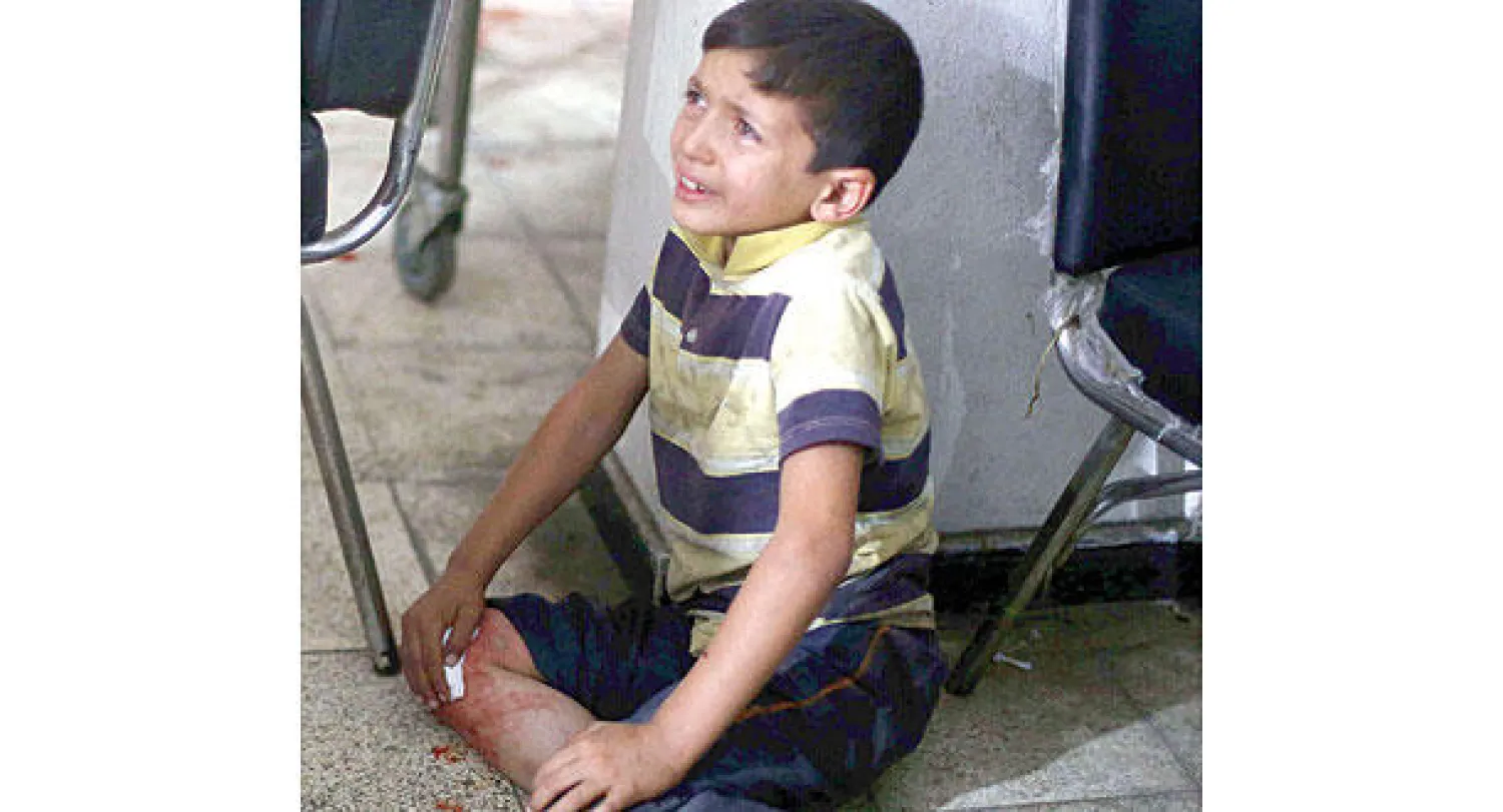 طفل سوري يبكي متأثرا بمشاهدة والده الجريح في مستشفى بدوما (أ.ف.ب)