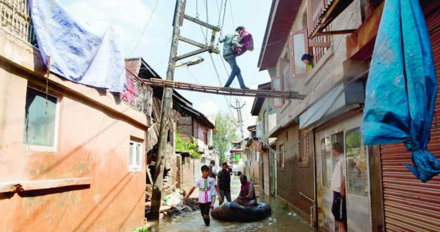 شاب ينقل حاجيات ذات قيمة من منزله المتضرر من الفيضانات إلى منزل جاره عبر سلم لتفادي الماء على الأرض في سريناغار أمس (أ.ب)