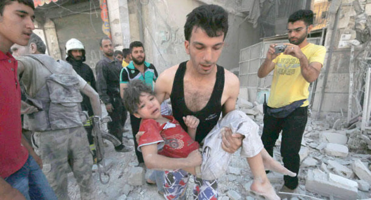 سوري يحمل طفلة مصابة بعد قصف قوات النظام السوري لمناطق في حلب بالبراميل المتفجرة أمس (رويترز)