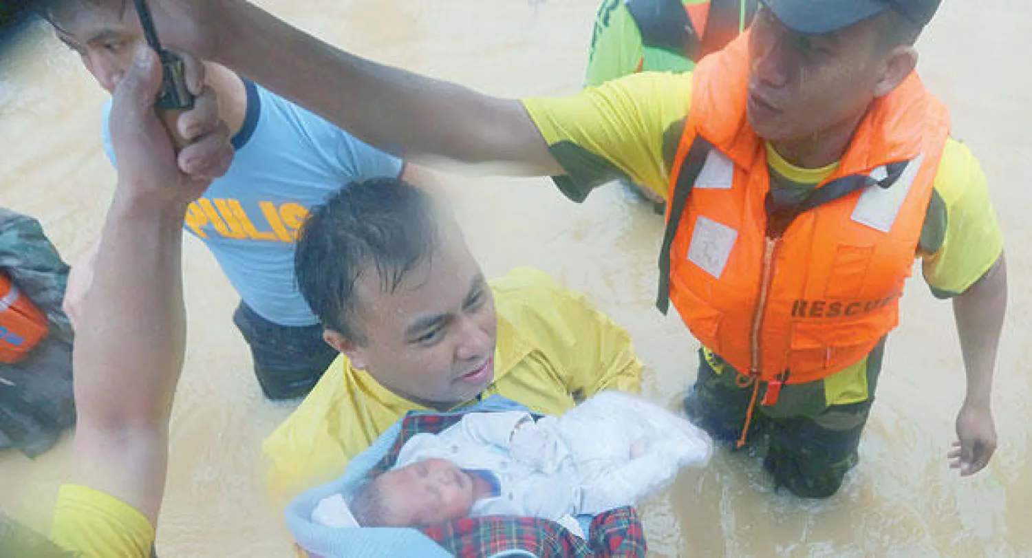 رجال الإنقاذ يحملون طفلا في قرية ماريكينا شمال العاصمة الفلبينية مانيلا التي ضربتها عاصفة استوائية (إ.ب.أ)