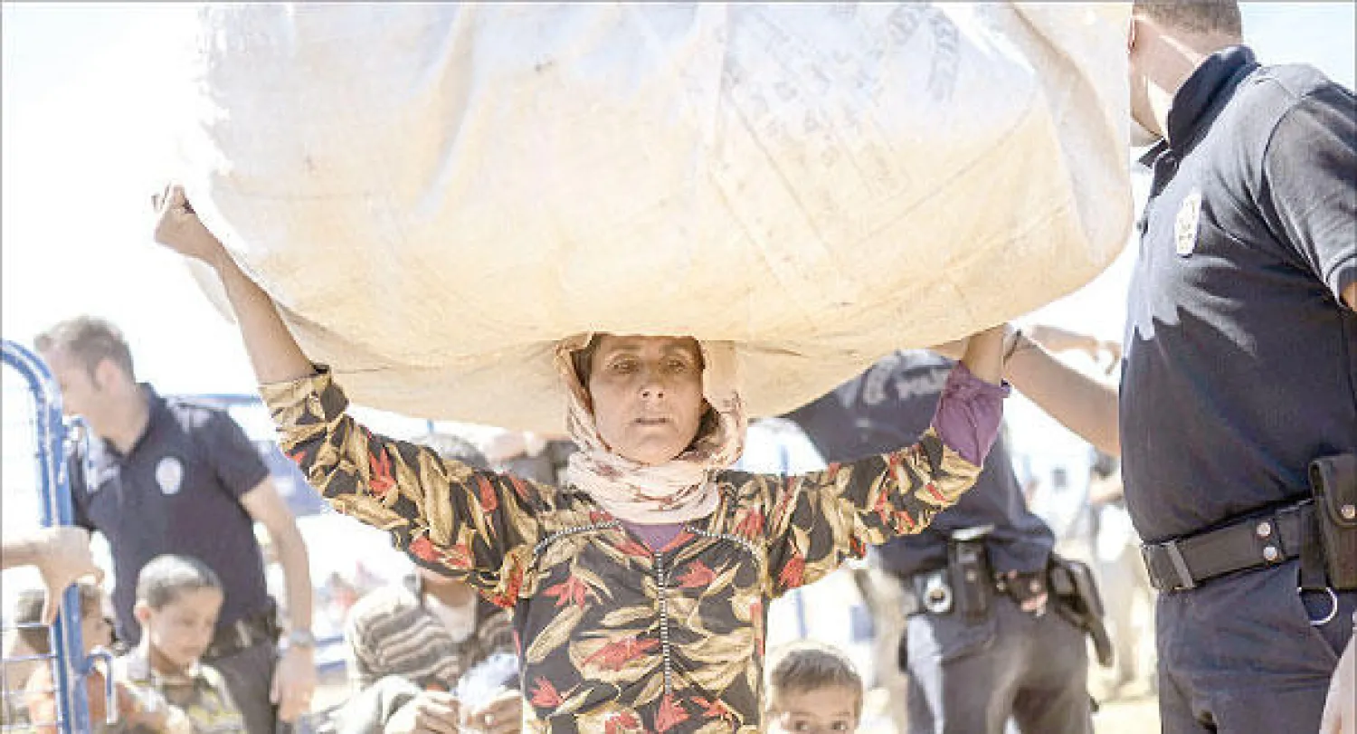 نازحة كردية سورية تحمل متاعها فوق رأسها وهي تعبر الحدود إلى تركيا أمس (أ.ف.ب)