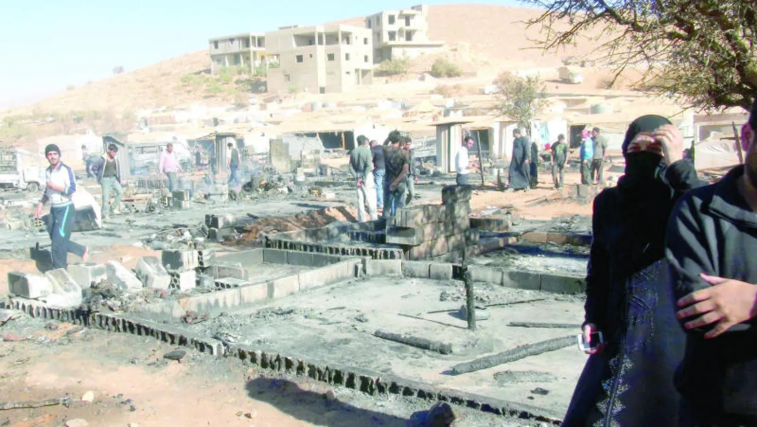 لاجئون سوريون يمرون فوق الخيام التي تعرضت للحرق في مخيم للاجئين بعرسال أمس (أ.ف.ب)