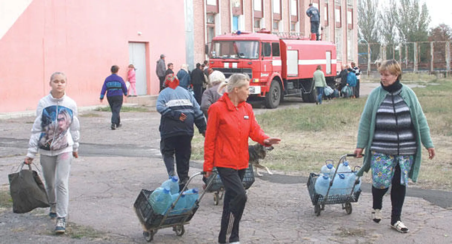 سكان يحملون أمس قوارير بلاستيكية ملأوها بالماء من ناقلة تابعة لجهاز الإطفاء في منطقة دونيتسك شرق أوكرانيا حيث يعانون أزمة ماء منذ 3 أشهر (إ.ب.أ)