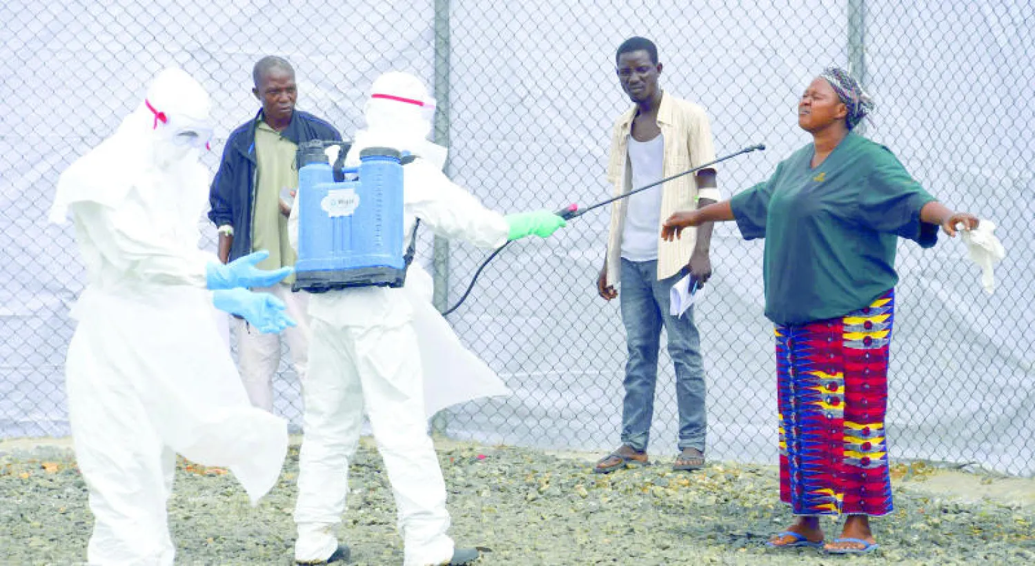 عنصر طبي يرش بالماء امرأة جلبت أشخاصاً مشتبها في إصابتهم بـ«إيبولا» كإجراء احترازي في مركز صحي بمونروفيا أمس (أ.ف.ب)