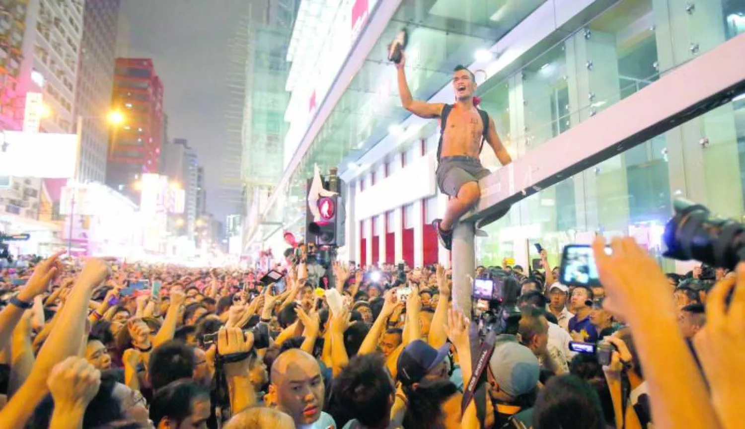 قيادي في الحركة الطلابية يصعد إلى أحد أعمدة إشارات المرور متحديا مجموعات طالبت المتظاهرين بمغادرة حي مونغ كوك التجاري في هونغ كونغ أمس (أ.ب)