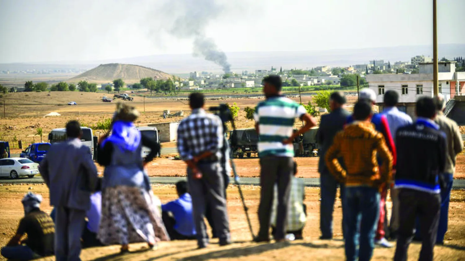 سوريون يراقبون تصاعد الدخان من مدينة كوباني على الحدود السورية - التركية والمحاصرة من قبل تنظيم {داعش} أمس (أ.ف.ب)