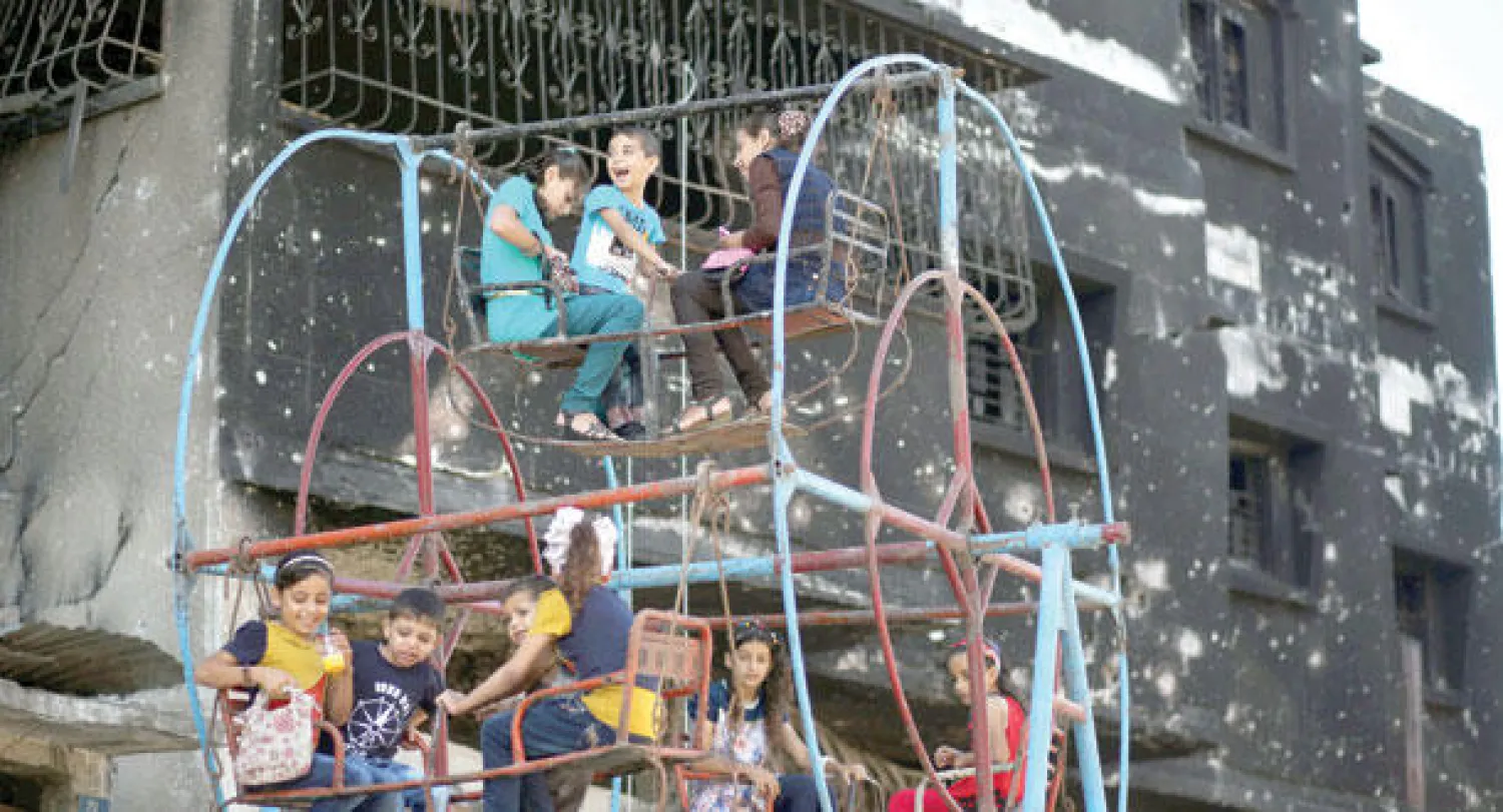 أطفال فلسطينيون من غزة يلعبون بأرجوحة أمام مبنى دمرته قوات الاحتلال الإسرائيلي احتفالا بعيد الأضحى المبارك (إ.ب.أ)