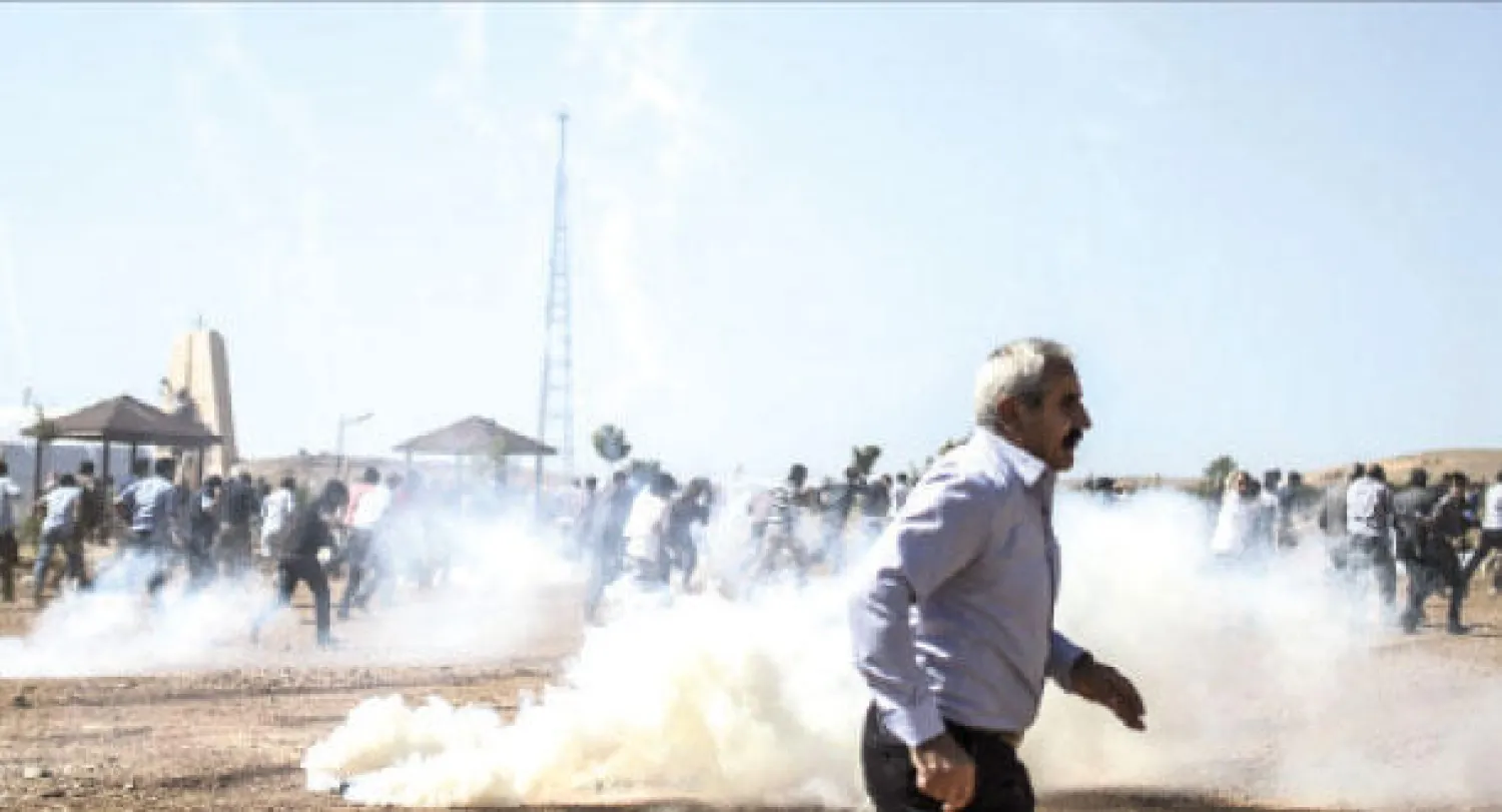 محتجون أكراد هاربون من الغاز المنبعث من القنابل المسيلة للدموع التي ألقاها الجنود الأتراك في مواجهات على الحدود التركية السورية أمس (أ.ف.ب)