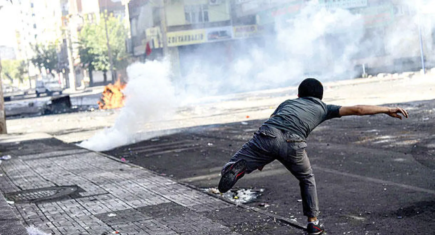 أحد المحتجين الأكراد يرمي حجارة تجاه سيارة شرطة أثناء الاحتجاجات ضد الحكومة جنوب تركيا أمس (أ.ف.ب)