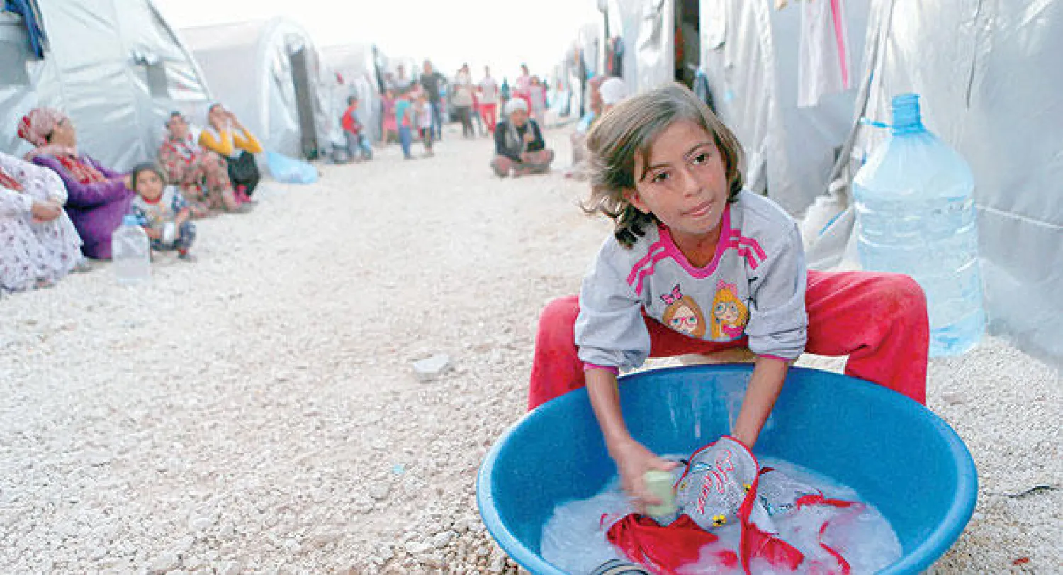 طفلة كردية تغسل الثياب في مخيم اللاجئين بمدينة سوروك التركية الحدودية أمس (رويترز)