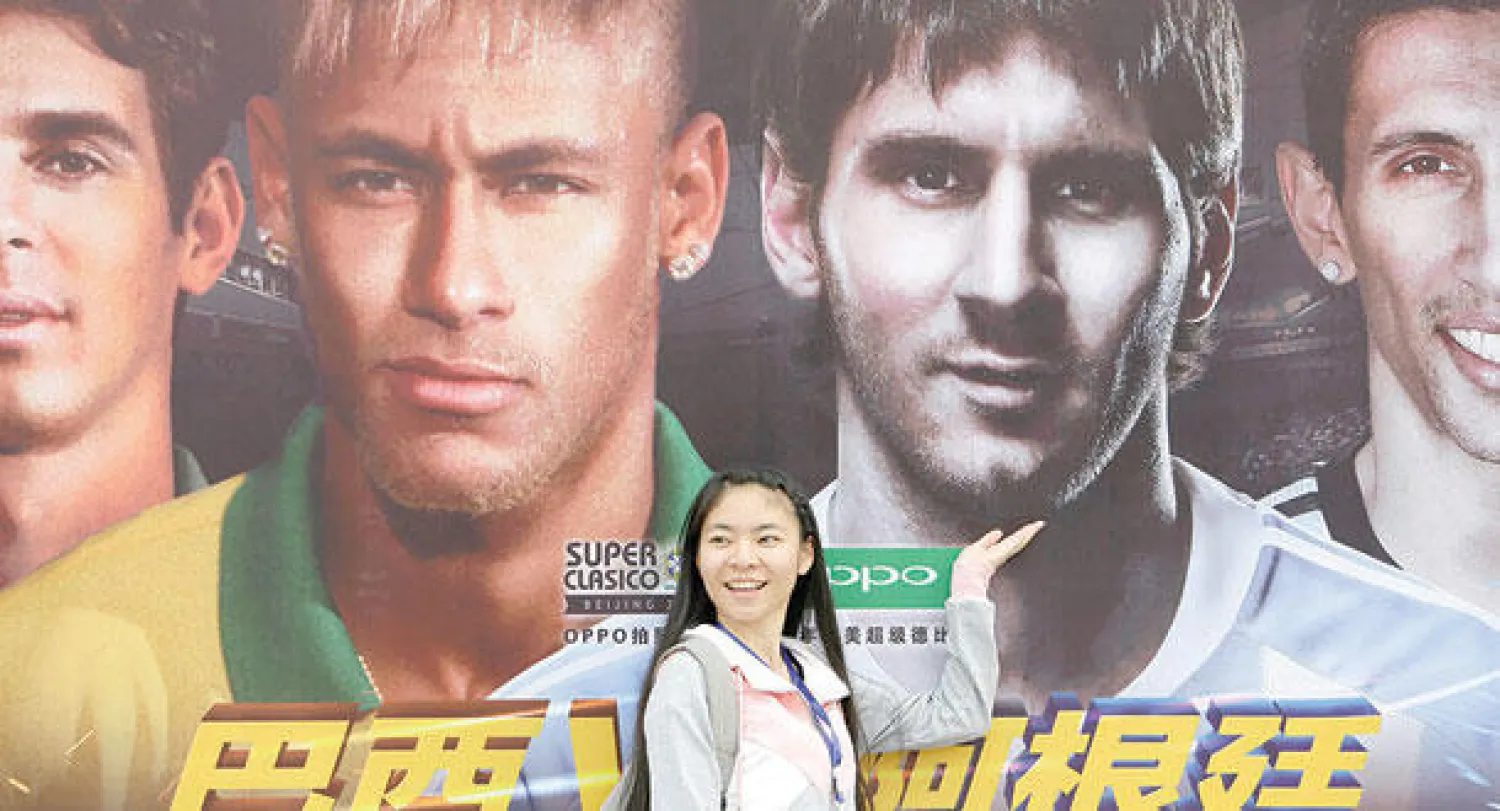 صينية تقف أمام ملصق ضخم للإعلان عن مواجهة ميسي ونيمار في قمة الأرجنتين والبرازيل اليوم (رويترز)