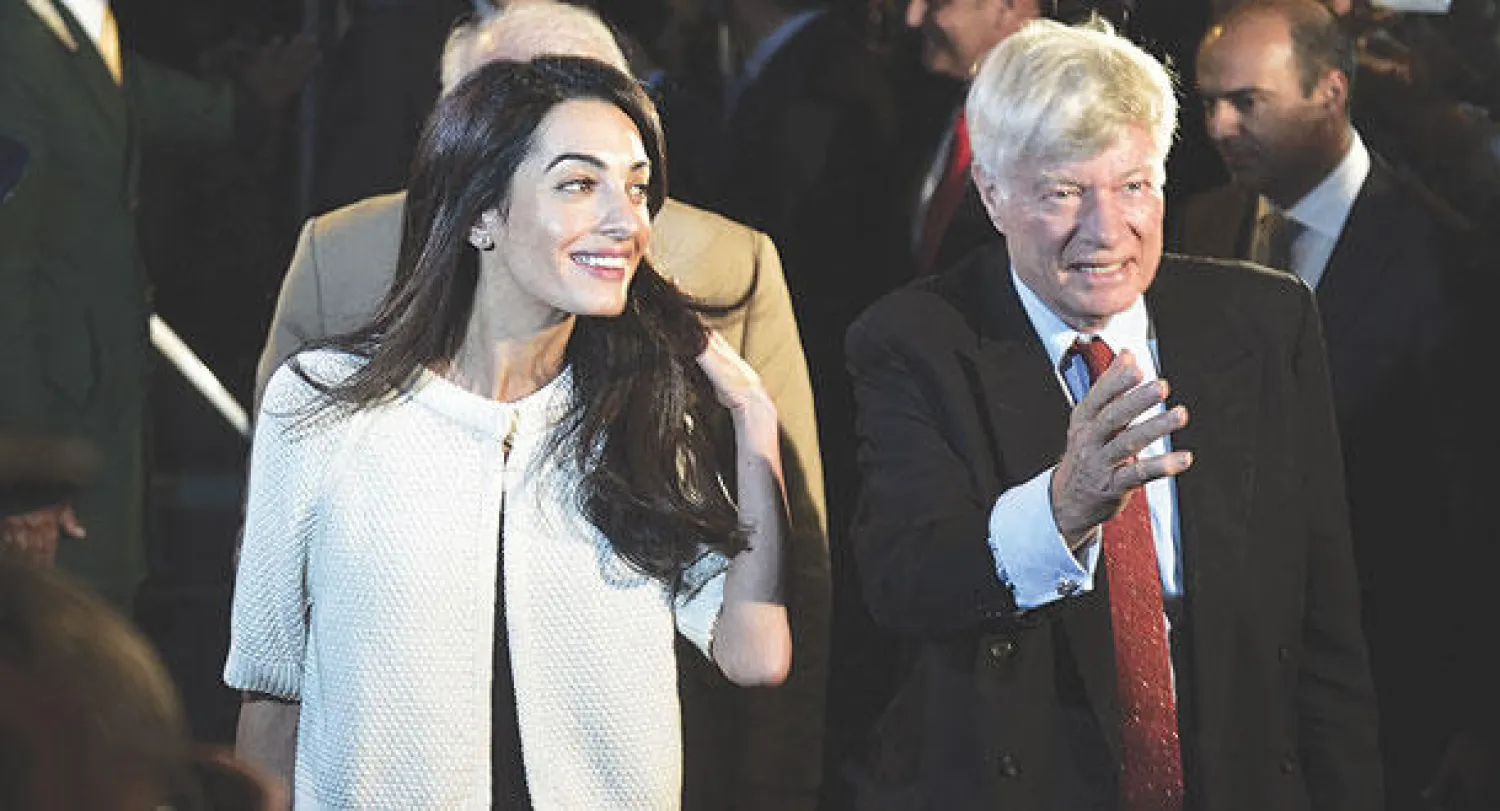 آمل علم الدين لدى وصولها إلى مطار أثينا بصحبة رئيسها جيفري روبرتسون (أ.ف.ب)