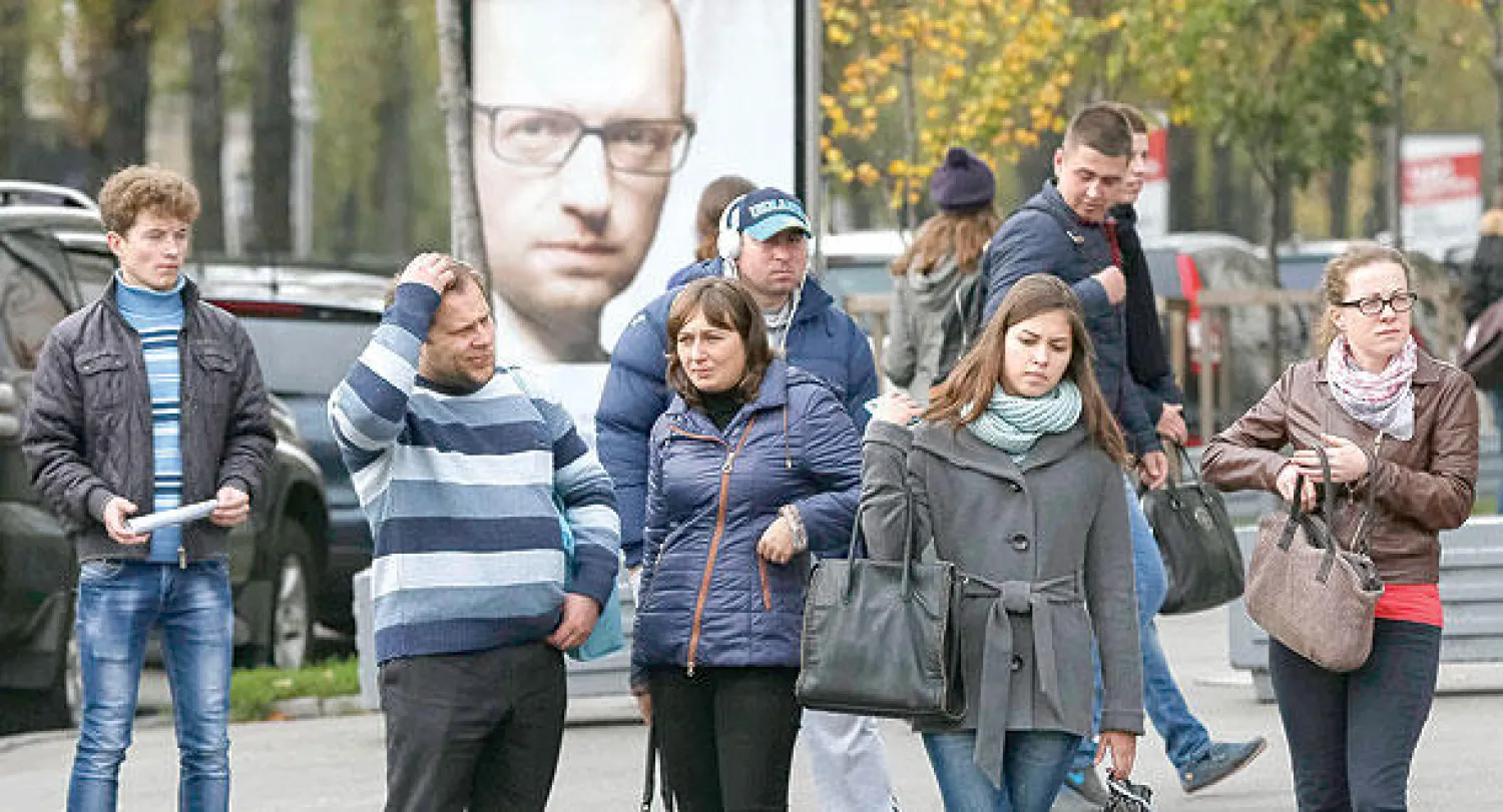 أوكرانيون يقفون أمام صورة دعائية لرئيس الوزراء أرسيني ياتسينيوك في كييف أمس استعدادا لانتخابات الأحد المقبل (رويترز)