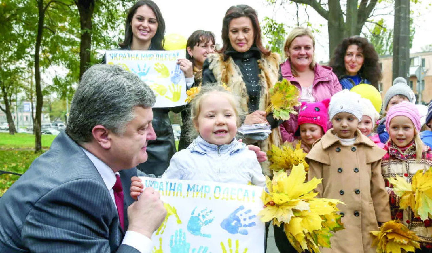 بوروشينكو يجلس إلى جانب أطفال خلال زيارته مدينة أوديسا على البحر الأسود أمس. وكتب على اللافتة المرفوعة «أوكرانيا، سلم، أوديسا» (رويترز)